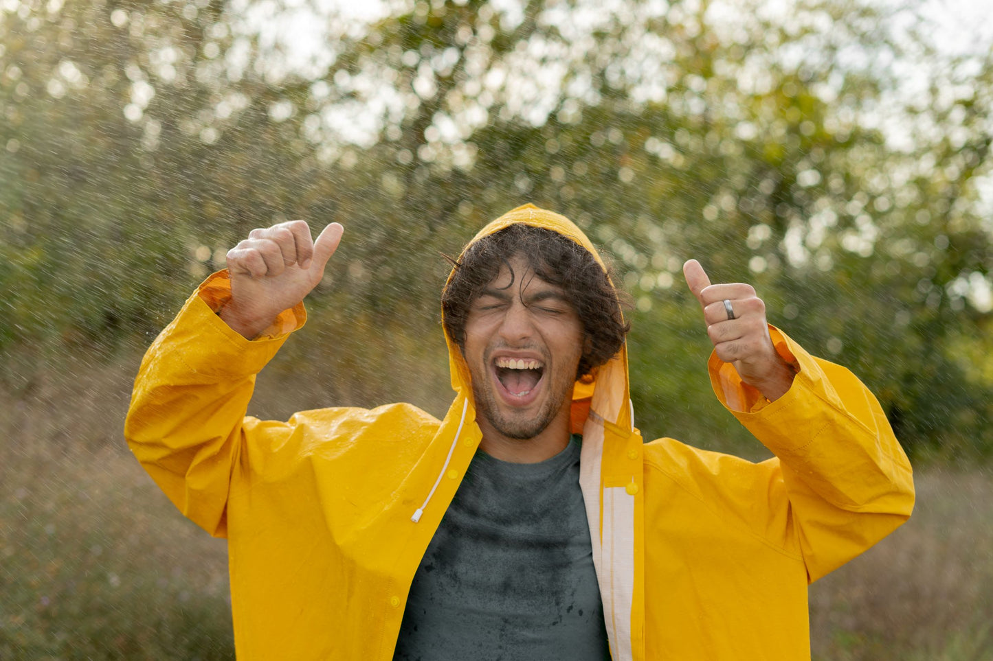 Person wearing a yellow raincoat with arms raised outdoors